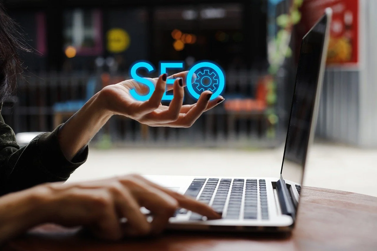 A person working on a laptop with a glowing SEO icon floating above their hand, representing digital marketing and search engine optimization